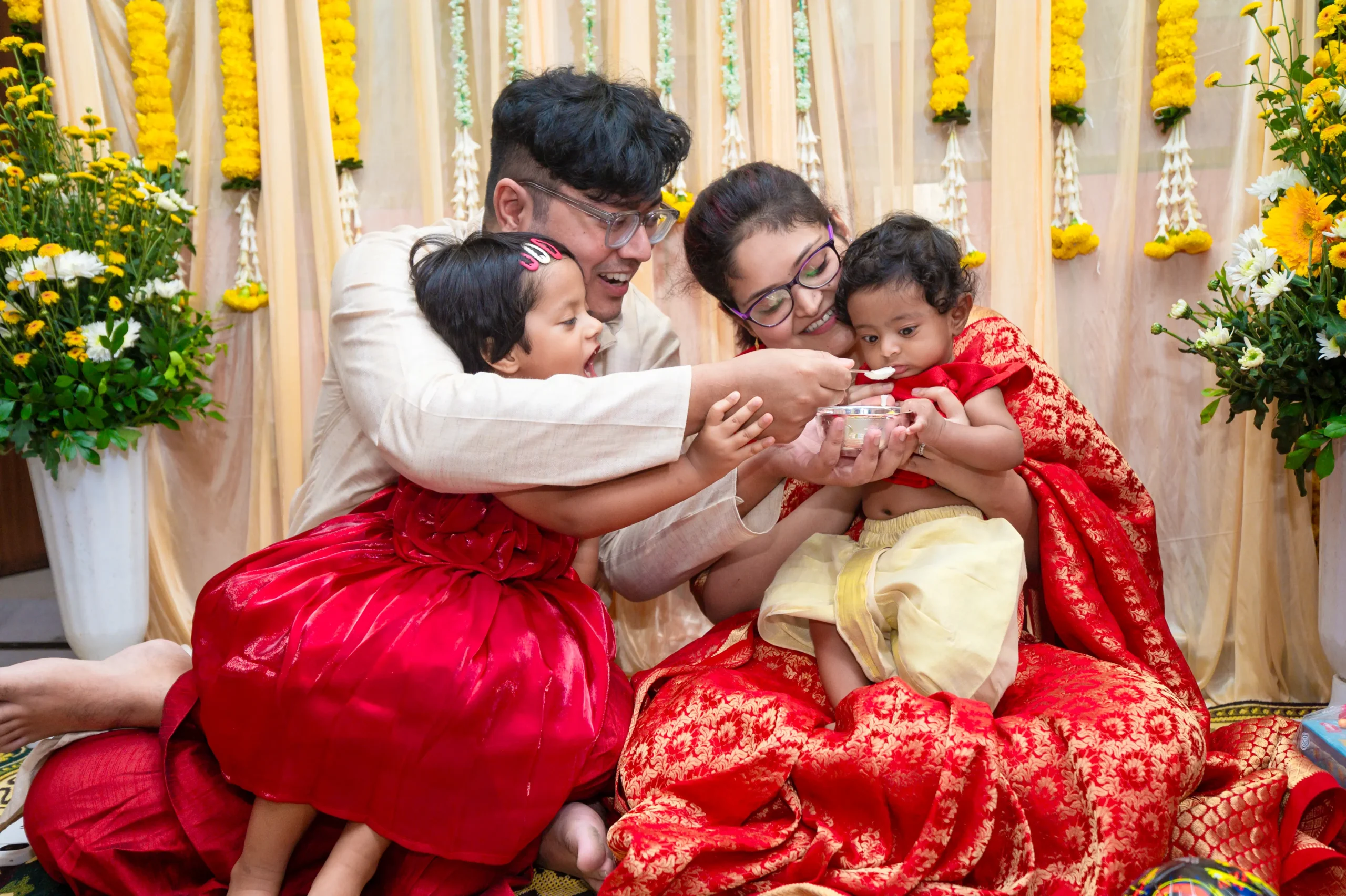 A family joyfully helping their baby eat during a traditional Bengali rice-feeding ceremony, captured during a Bengali Annaprashan Photography session by Golden Memories.